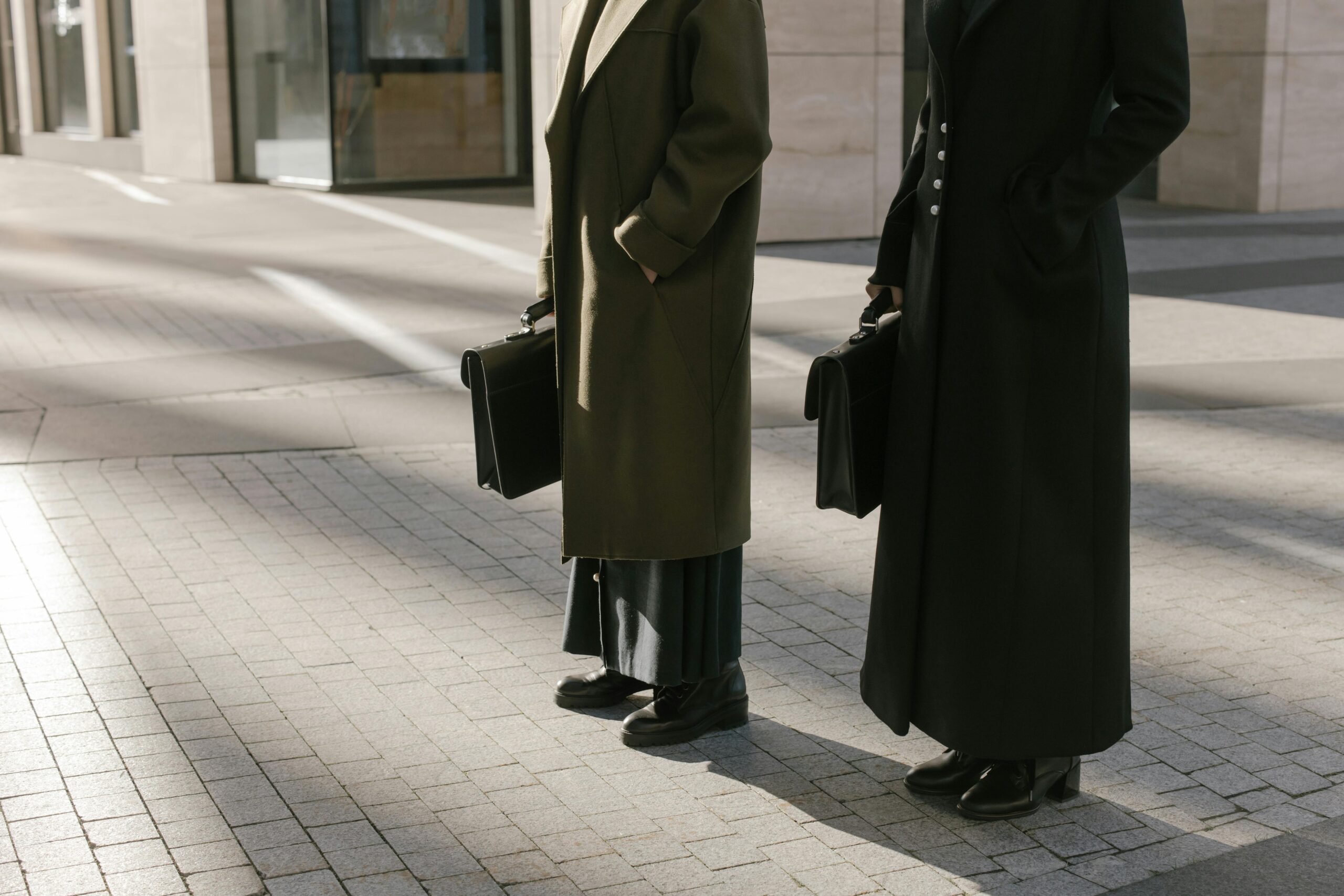 Two business professionals standing outdoors with briefcases, exuding elegance and professionalism.